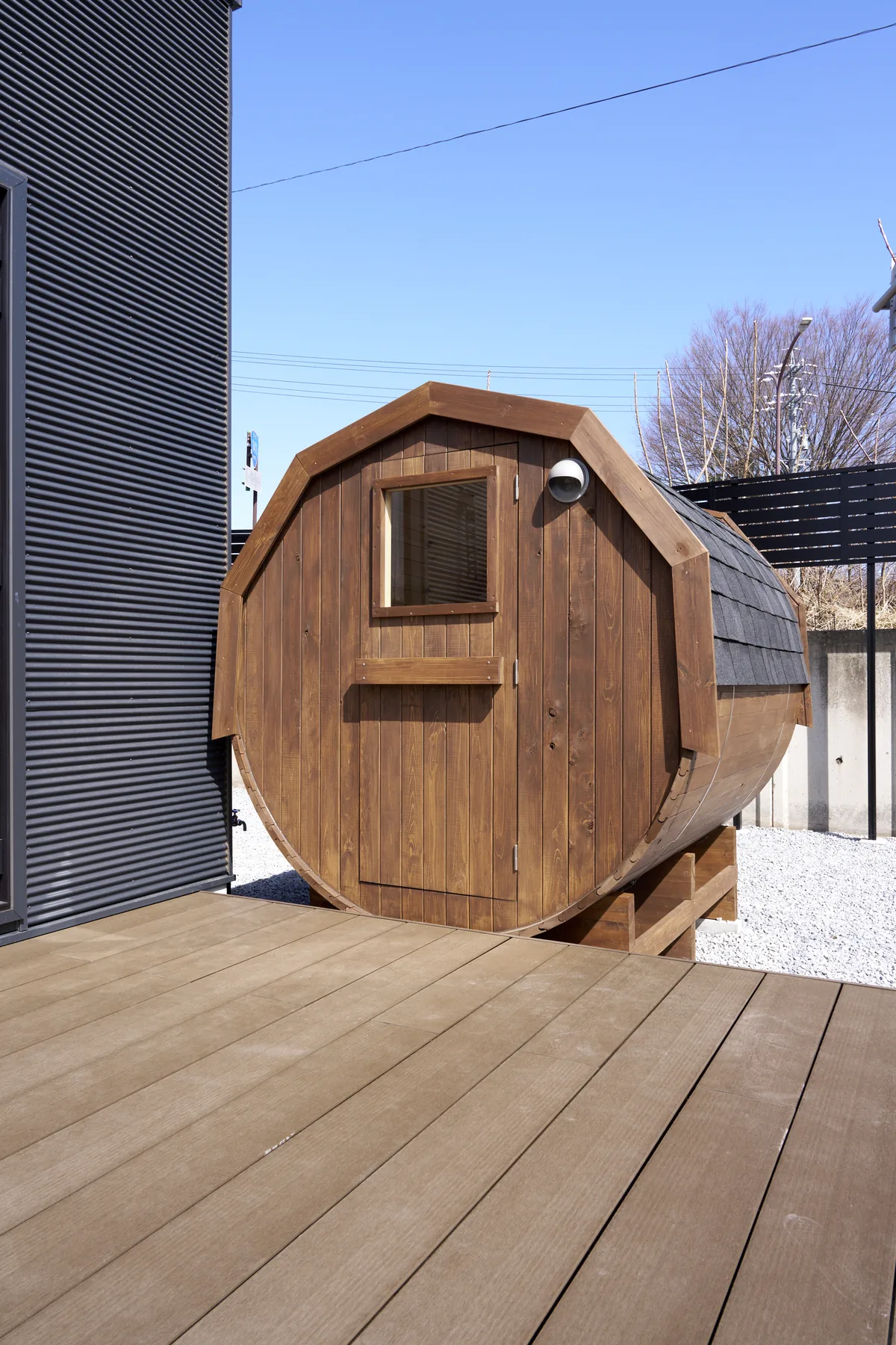 住宅のウッドデッキに設置したダークカラーのバレルサウナ